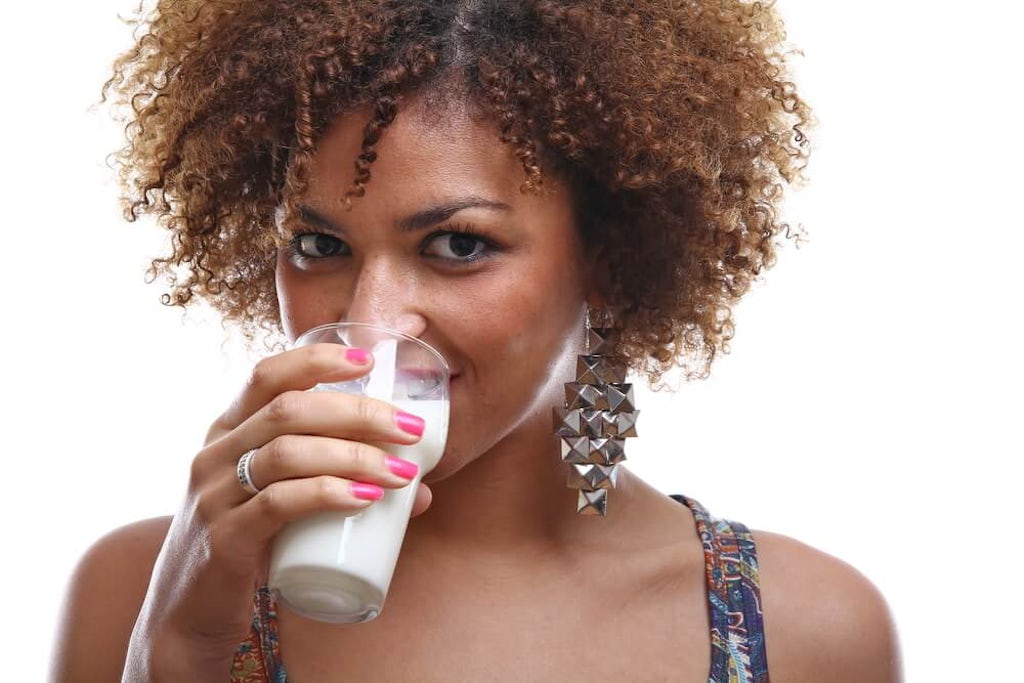 A woman drinks milk from a glass while smiling at the camera