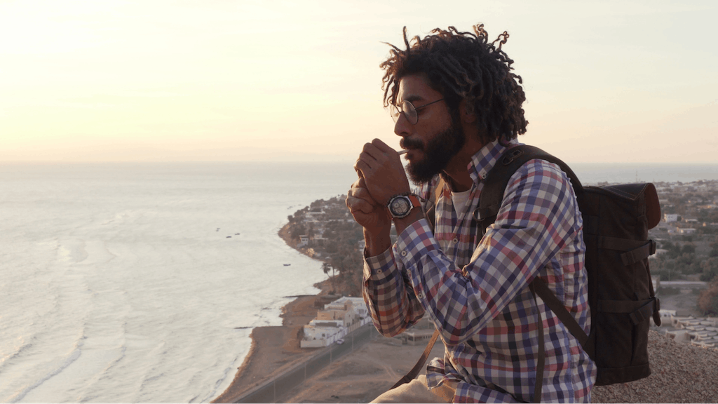 Man smoking joint with cannabis sitting on a cliff at sunrise