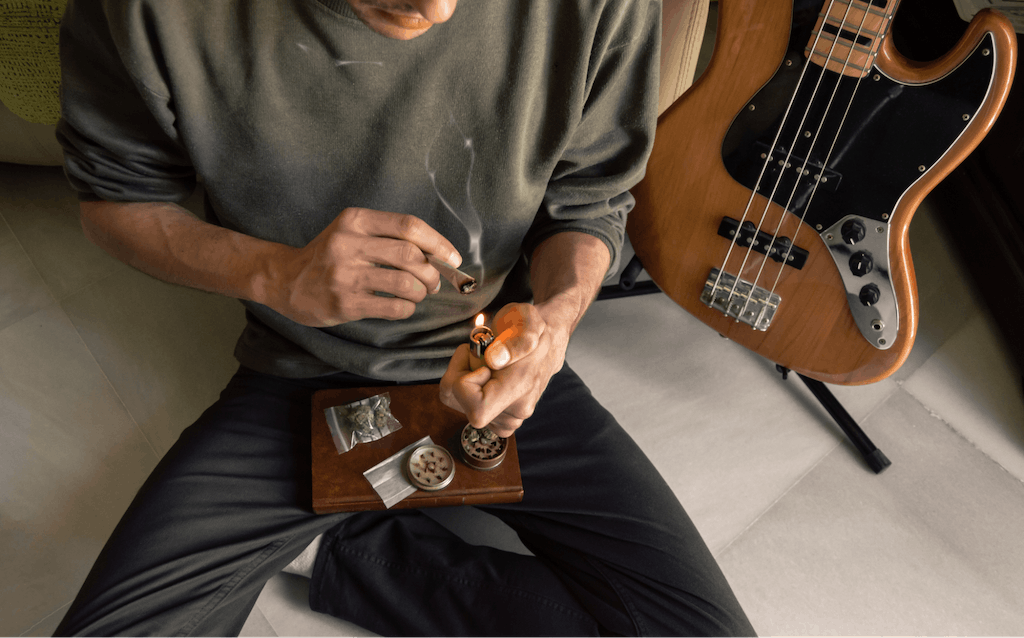 Man sitting on the floor smoking a marijuana joint at home after playing the bass.